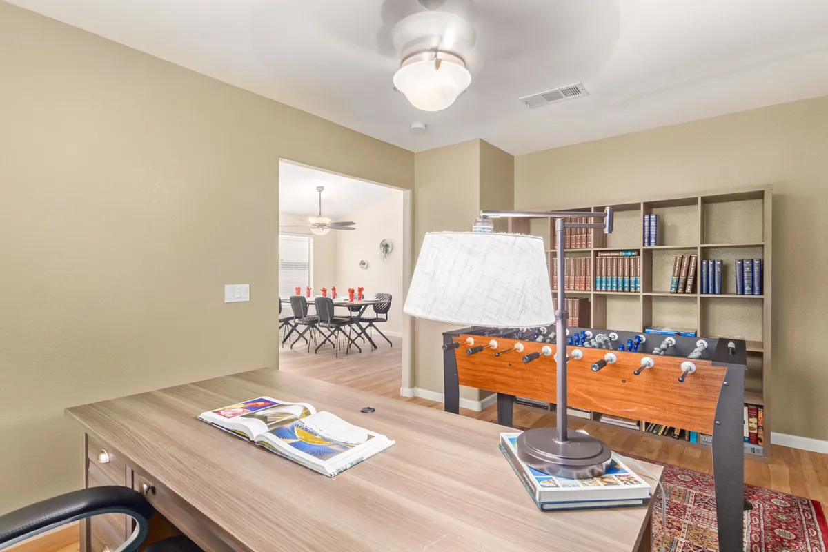 This image features a dedicated room with a desk and lamp for focused work, a foosball table for recreation, and a bookshelf that adds both storage and a casual, lived-in feel. The space is designed to easily transition between productivity and play, providing visual cues for both office and game room purposes.