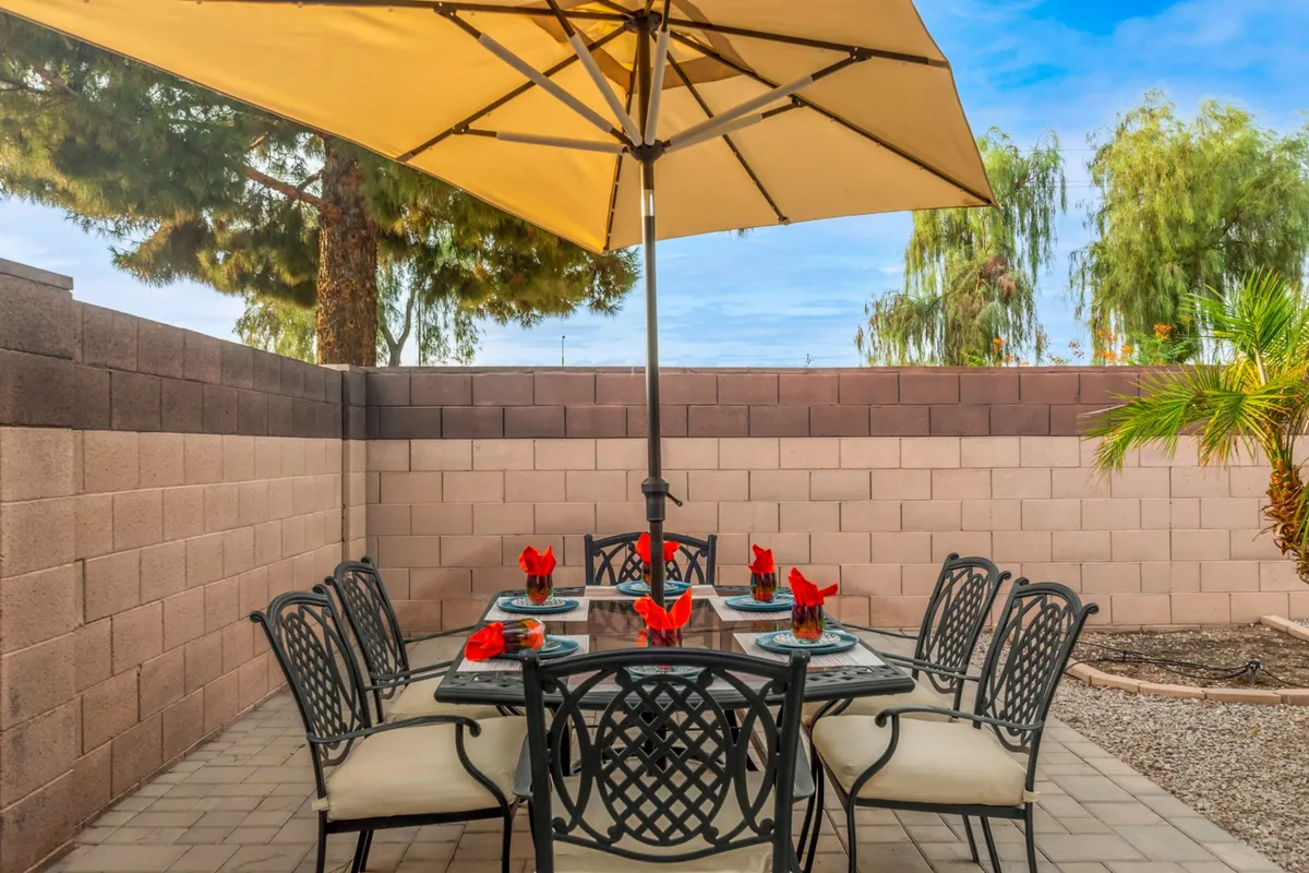 An outdoor dining area featuring a table with a bright umbrella and decorative flowers, set in a welcoming patio space. The area suggests opportunities for al fresco meals and socializing in a dog-friendly environment.