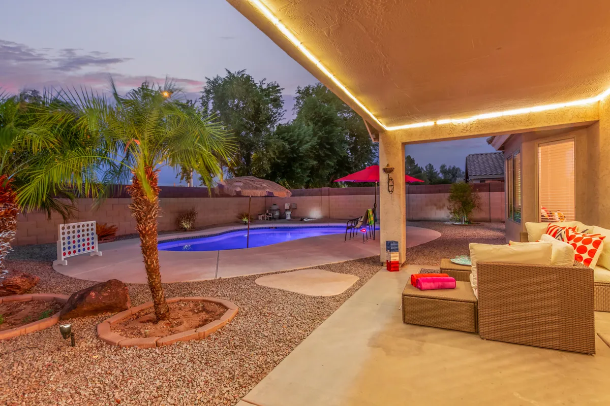 This exterior image showcases a sparkling swimming pool surrounded by palm trees and a well-appointed seating area. Soft outdoor lighting suggests both daytime relaxation and inviting sunset or evening gatherings.