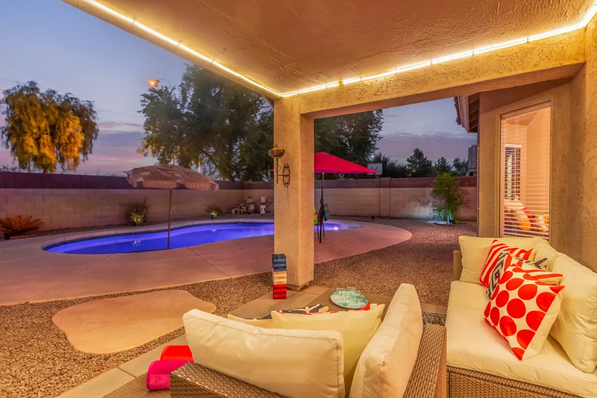 A sparkling swimming pool surrounded by outdoor seating and decorated with colorful pillows and a large umbrella. The area looks tranquil and inviting, perfect for a refreshing break or socializing after work.