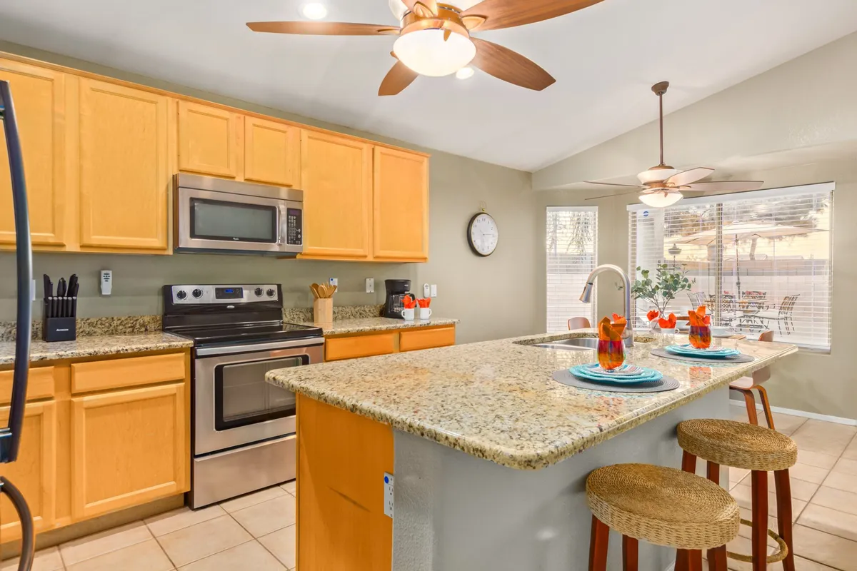 A bright, open kitchen with a granite countertop island featuring comfortable bar seating. Stainless steel appliances and natural light from large windows make the space feel both modern and inviting. The kitchen seamlessly connects with the surrounding living and dining areas, highlighting the open-concept layout.
