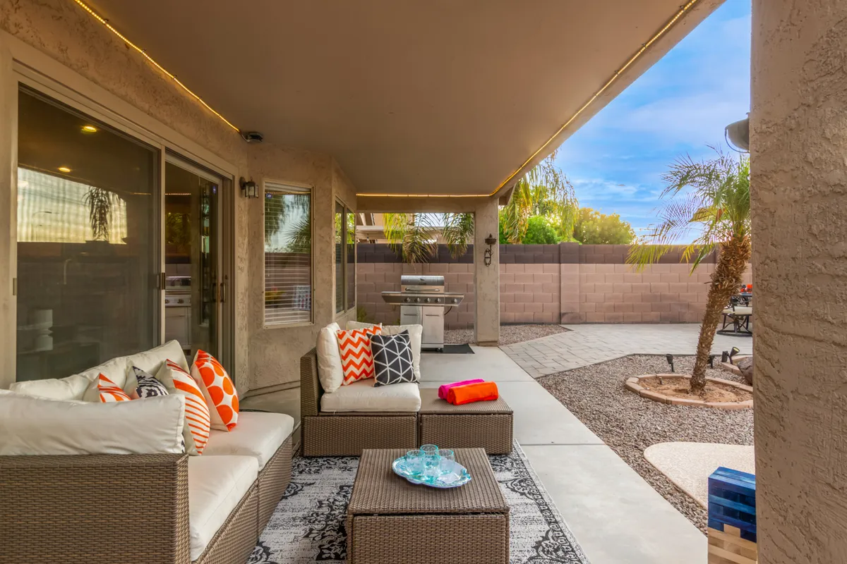 A welcoming outdoor seating area with decorative pillows is featured alongside a grill and palm trees, perfect for casual outdoor dining and lively social gatherings. String lights add a touch of nighttime ambiance.