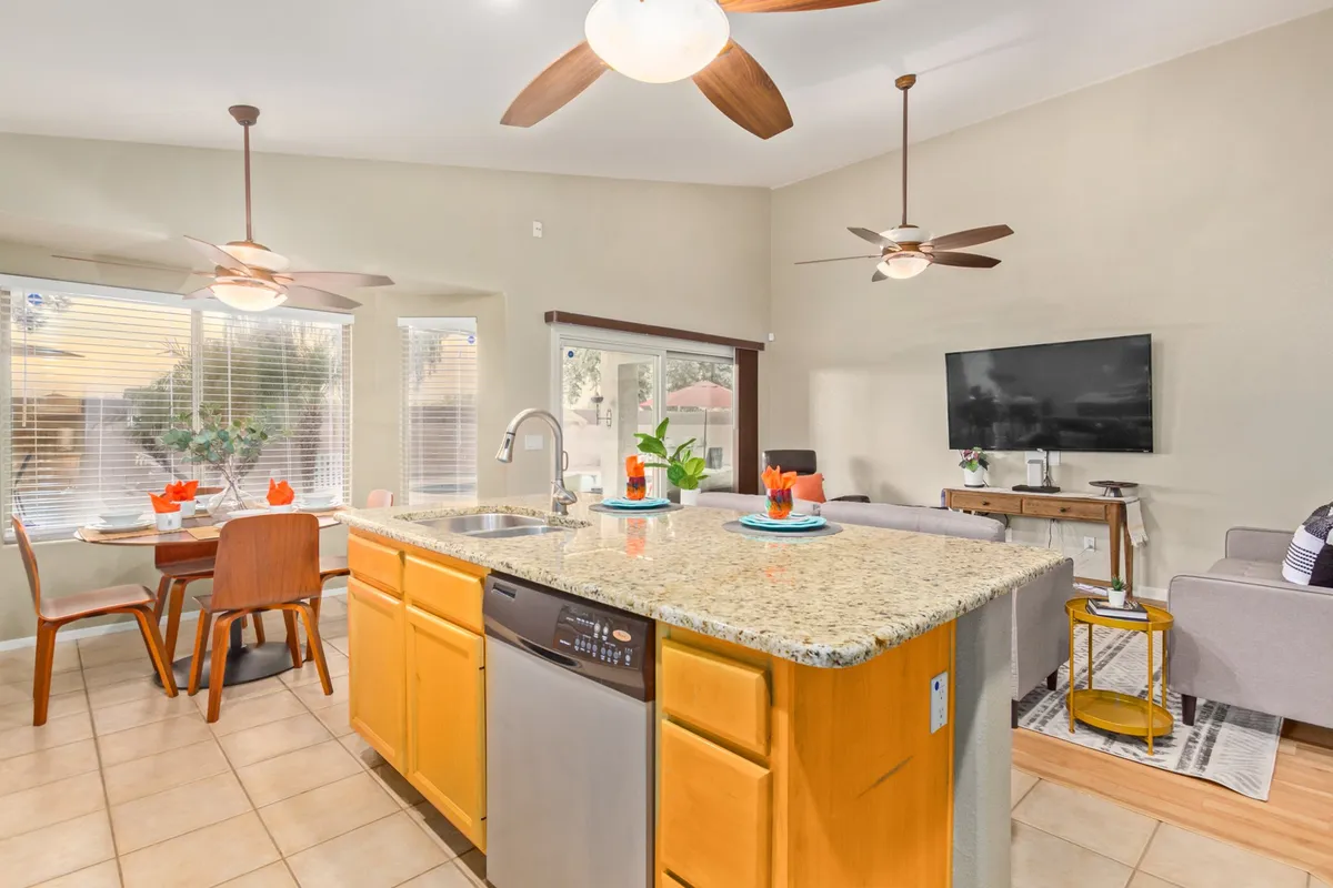 A spacious, open-concept area that combines a granite kitchen island, a dining table adorned with flowers, and a cozy family room with a TV. The layout encourages fluid interaction between cooking, dining, and lounging, embodying the great room's multifunctional spirit.