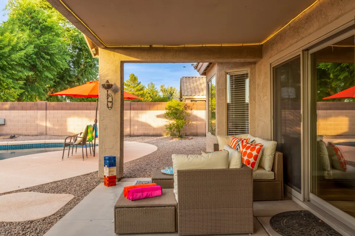 This exterior scene highlights a cheerful poolside area with colorful cushions, ample seating, and red umbrellas, all oriented around the swimming pool. The space feels vibrant and inviting for groups or couples.