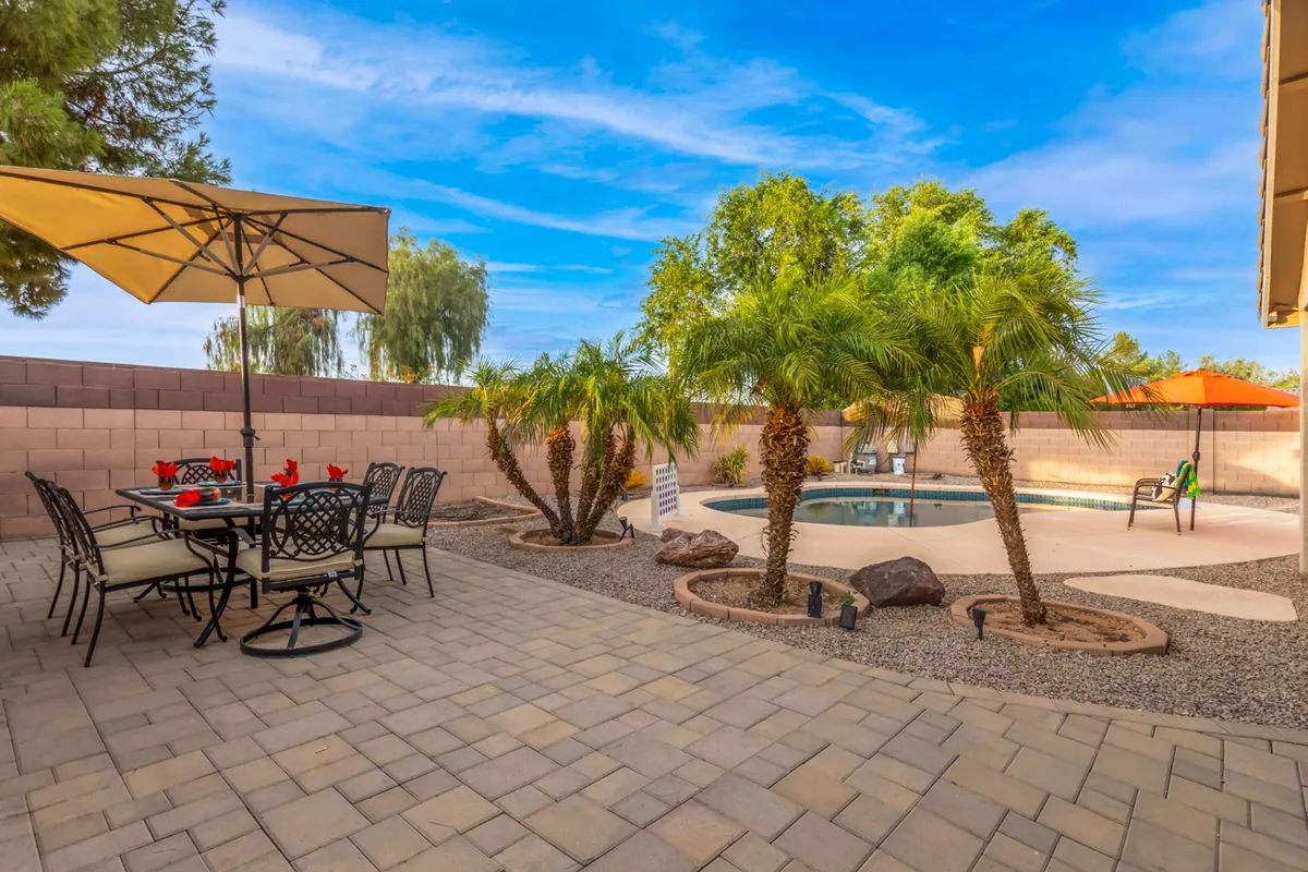 A serene backyard scene with a swimming pool, a dining table set for gatherings, palm trees, and an outdoor umbrella. The ambiance is cheerful and tranquil, inviting families to relax, dine, and enjoy the outdoors together.