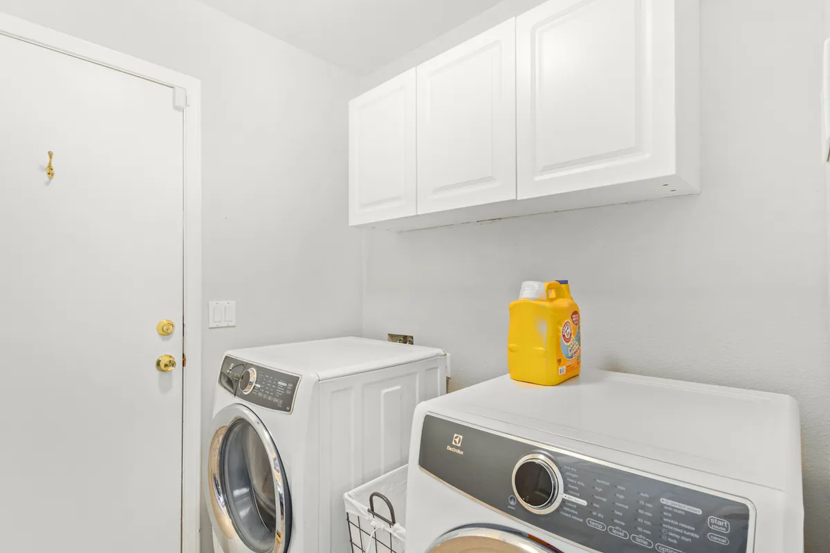 A practical and efficient laundry room with a washing machine, dryer, storage cabinet, and laundry detergent neatly arranged. The space is organized and designed for everyday convenience, making chores feel easy and accessible.